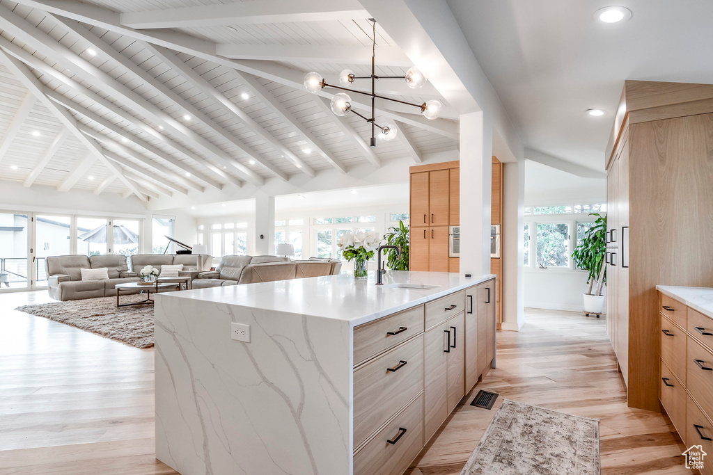 Kitchen featuring an island with sink, lofted ceiling with beams, and a healthy amount of sunlight