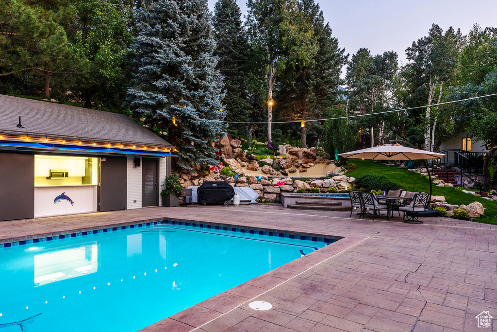 Pool at dusk featuring cooling unit, grilling area, and a patio area