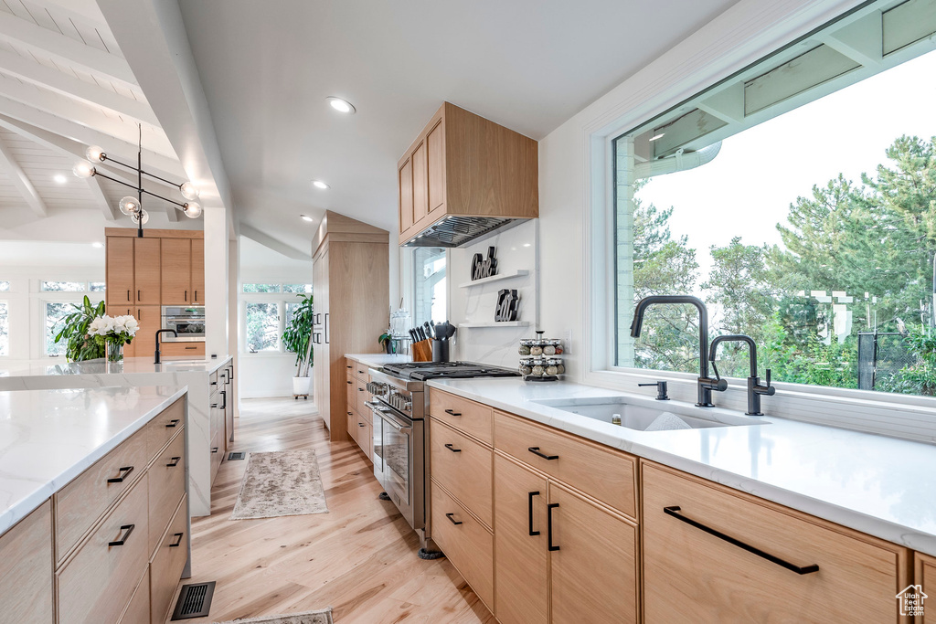 Kitchen featuring pendant lighting, sink, stainless steel stove, lofted ceiling with beams, and light wood-type flooring