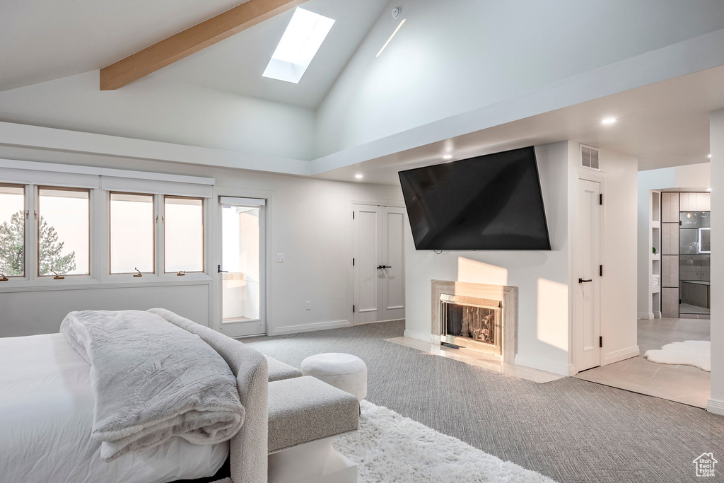 Bedroom featuring beam ceiling, light carpet, high vaulted ceiling, a skylight, and ensuite bathroom