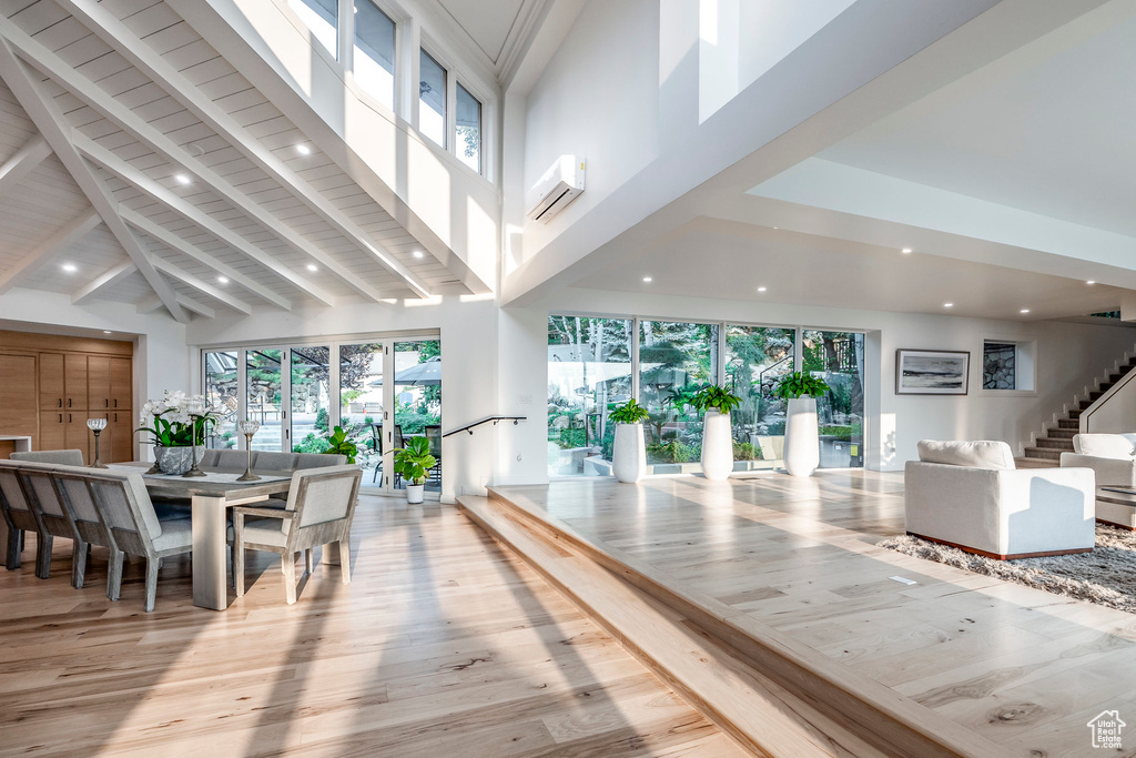 Dining space with high vaulted ceiling, beamed ceiling, light wood-type flooring, a skylight, and a wall mounted air conditioner