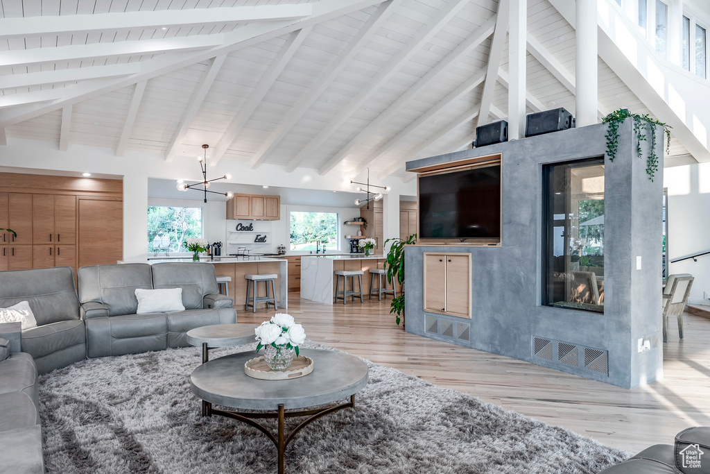 Living room featuring a notable chandelier, light wood-type flooring, beamed ceiling, and high vaulted ceiling