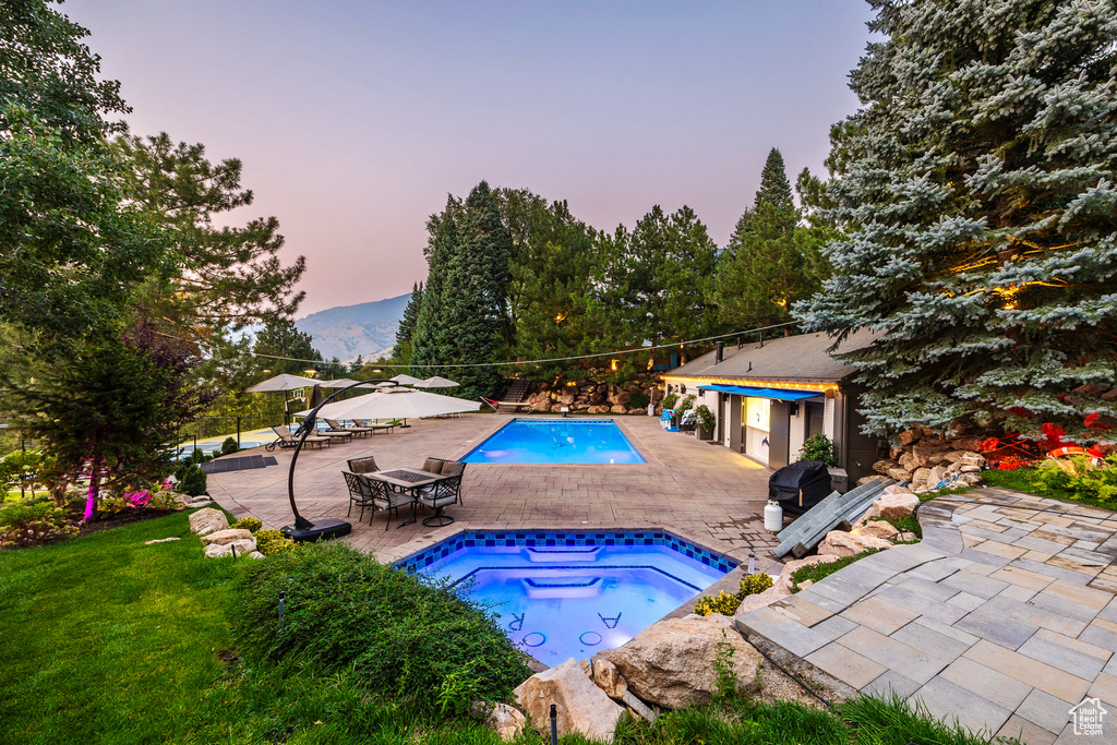 Pool at dusk with an in ground hot tub, a lawn, and a patio area