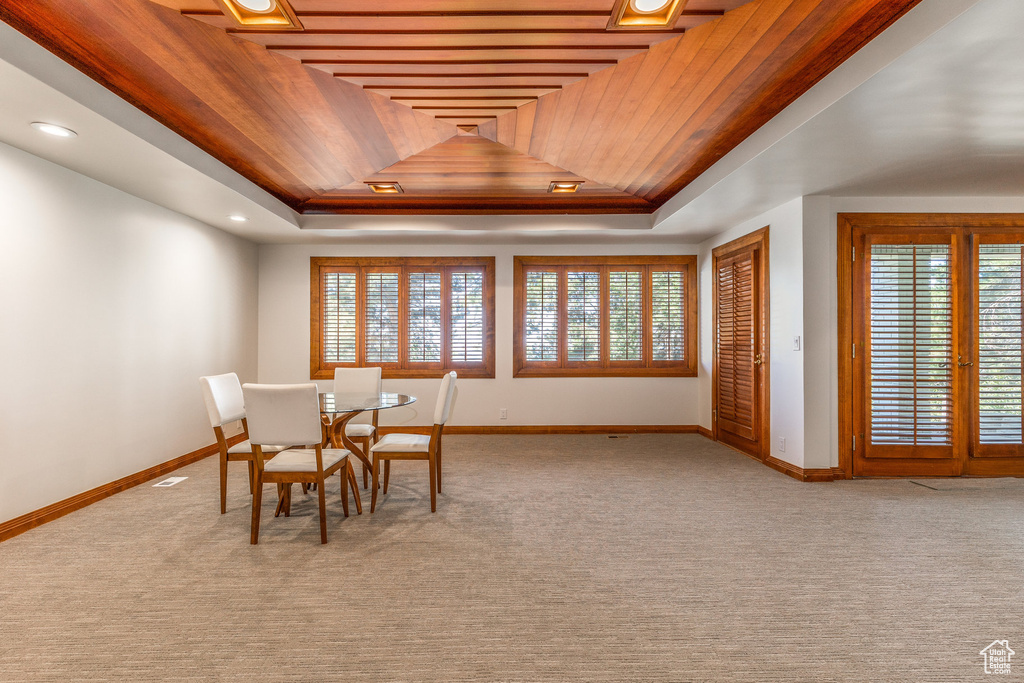 Carpeted dining area featuring a tray ceiling, wooden ceiling, and a healthy amount of sunlight