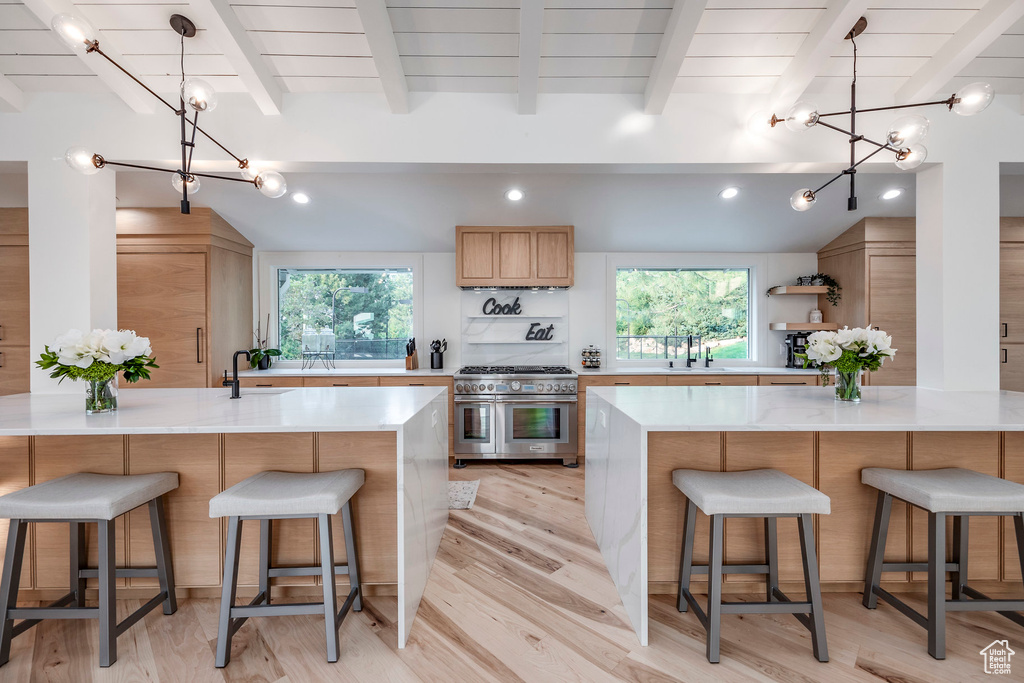 Kitchen with lofted ceiling with beams, a chandelier, kitchen peninsula, light hardwood / wood-style flooring, and double oven range