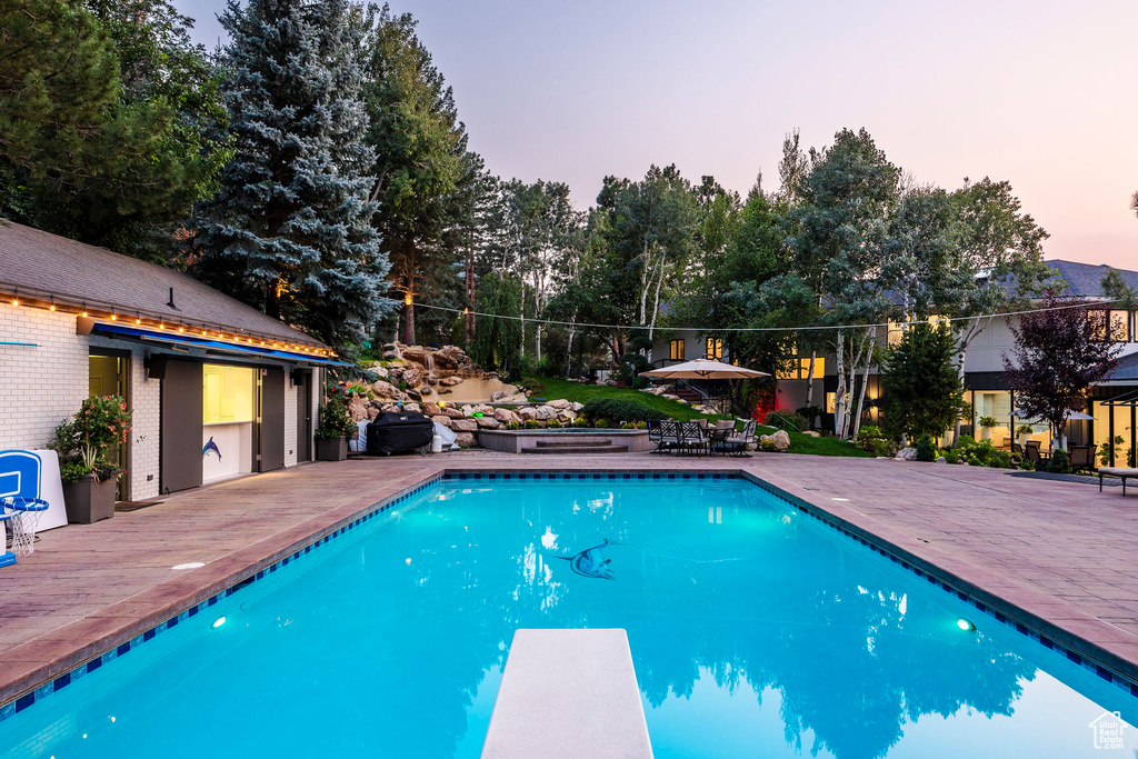 Pool at dusk featuring a diving board and a patio