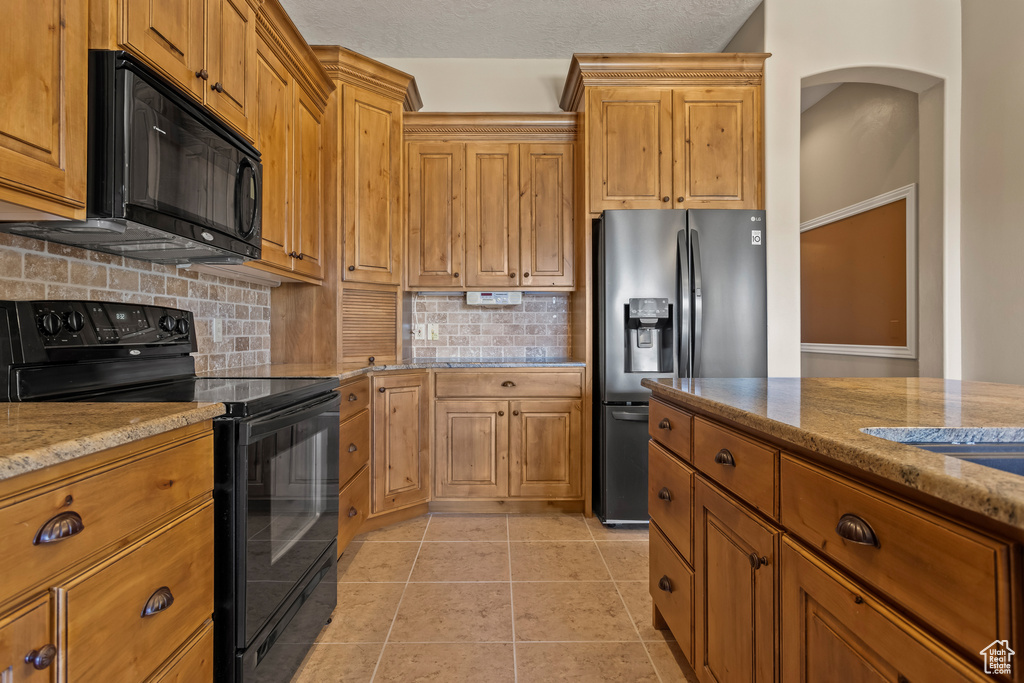 Kitchen with light stone counters, a textured ceiling, tasteful backsplash, black appliances, and light tile patterned floors