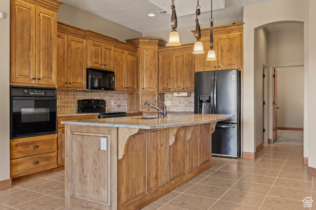 Kitchen with a textured ceiling, black appliances, a kitchen island with sink, and light tile patterned floors