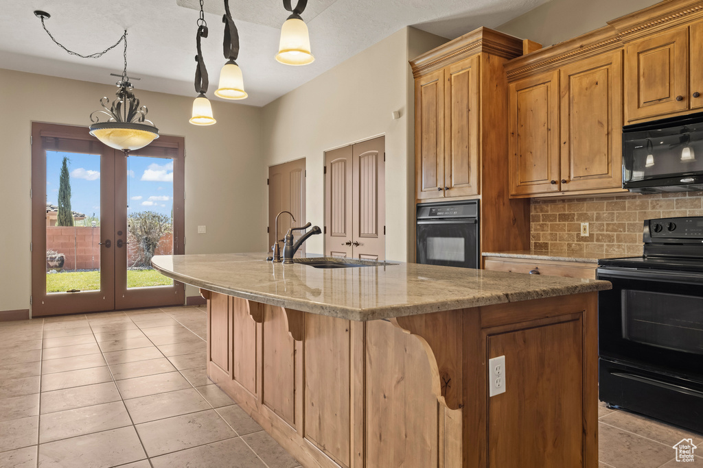 Kitchen featuring an island with sink, hanging light fixtures, tasteful backsplash, black appliances, and light stone countertops