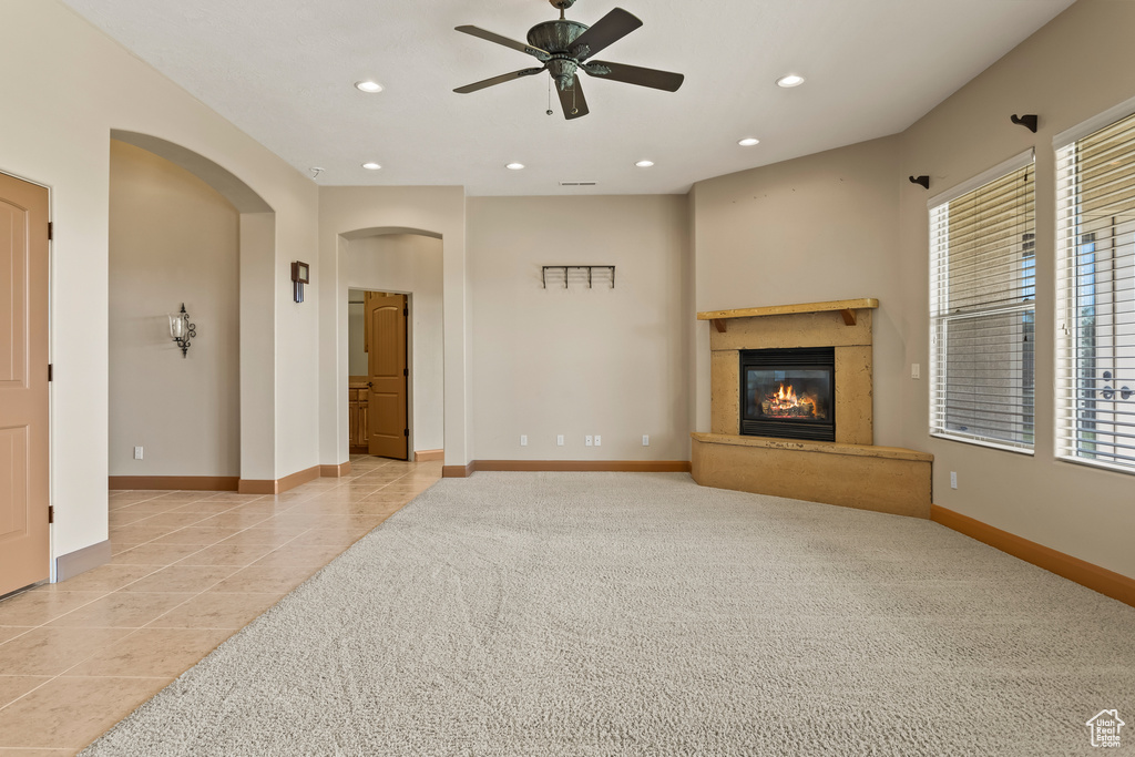 Unfurnished living room featuring ceiling fan, light colored carpet, and a high end fireplace