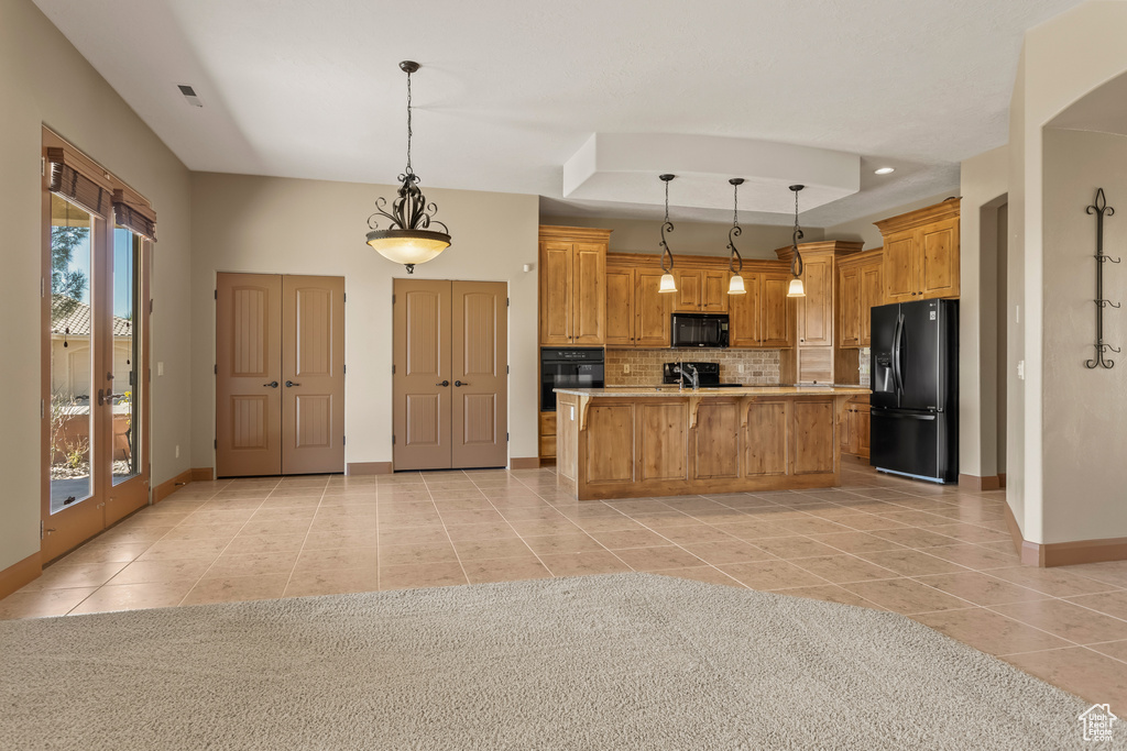 Kitchen with decorative light fixtures, light tile patterned flooring, a center island with sink, and black appliances