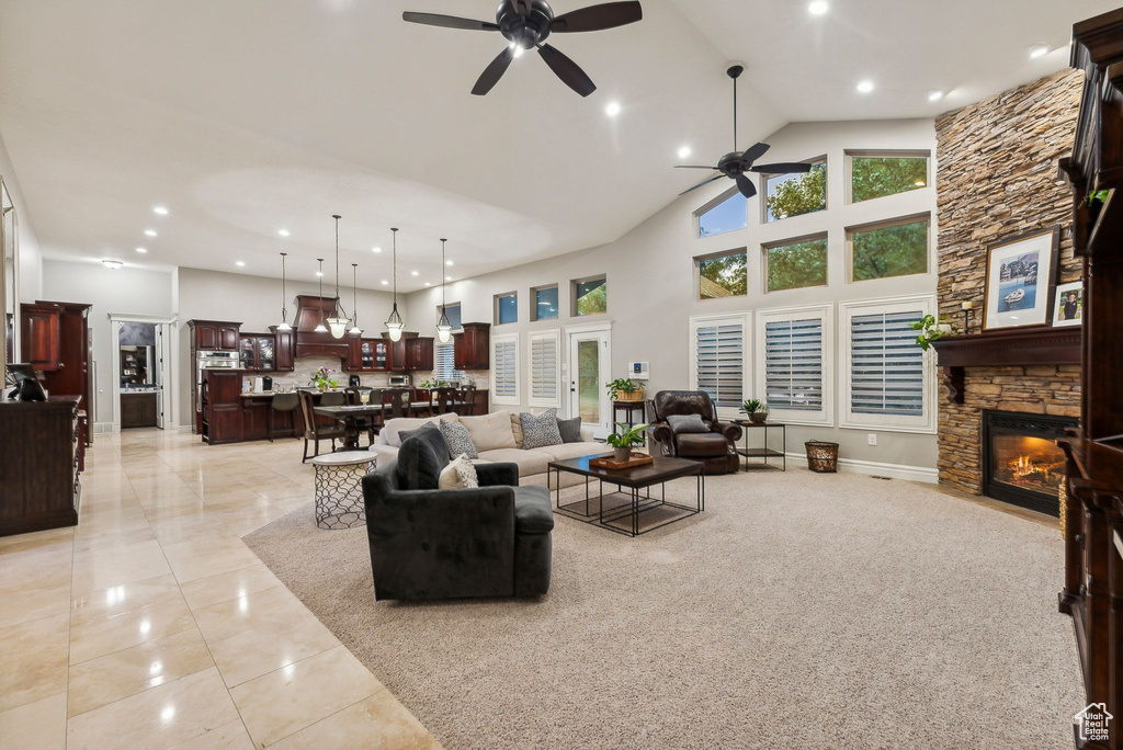 Living room featuring high vaulted ceiling, ceiling fan, light tile patterned floors, and a stone fireplace