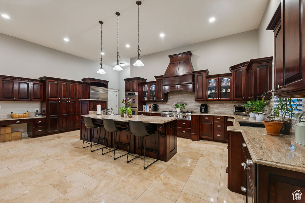 Kitchen with custom range hood, a breakfast bar, stainless steel appliances, a high ceiling, and a center island with sink