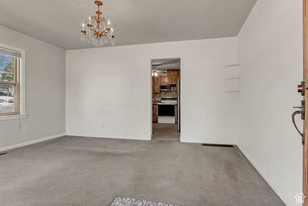 Spare room with ceiling fan with notable chandelier and carpet flooring