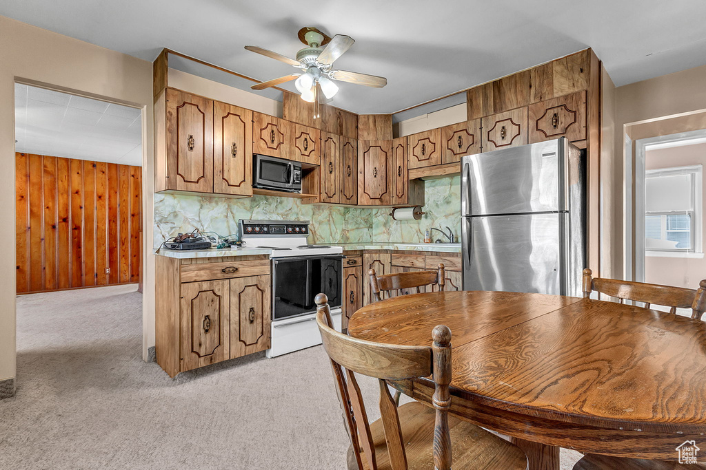 Kitchen featuring wood walls, light carpet, backsplash, appliances with stainless steel finishes, and ceiling fan