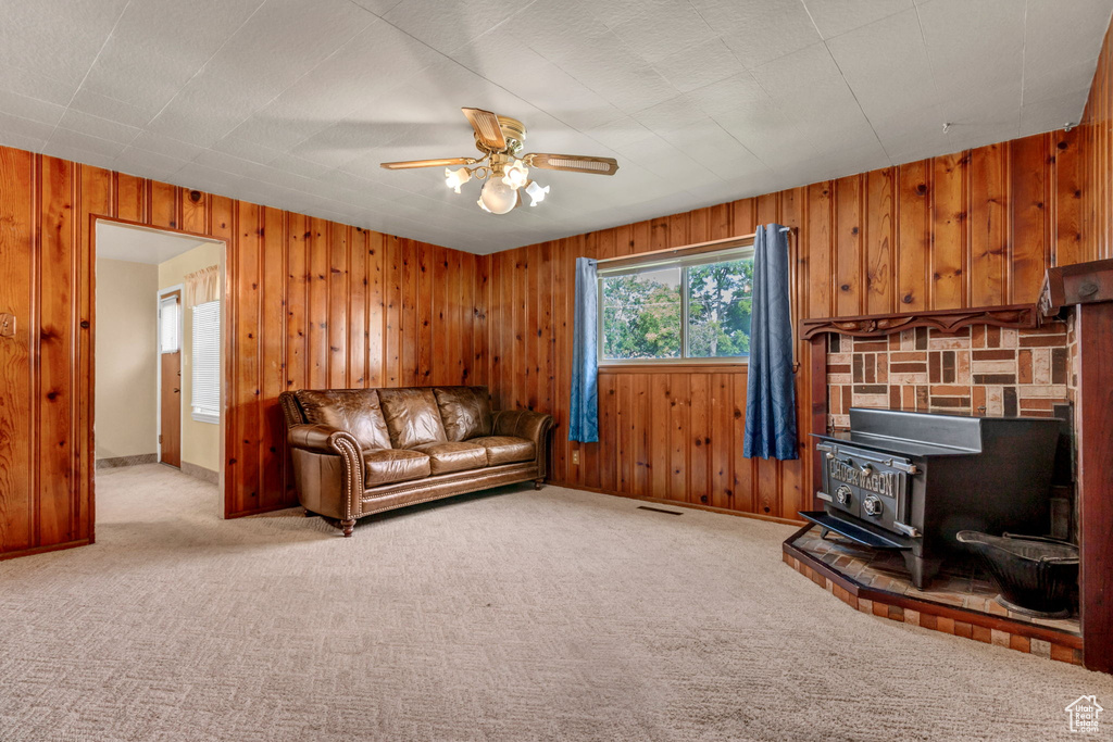 Carpeted living room featuring a wood stove, wood walls, and ceiling fan