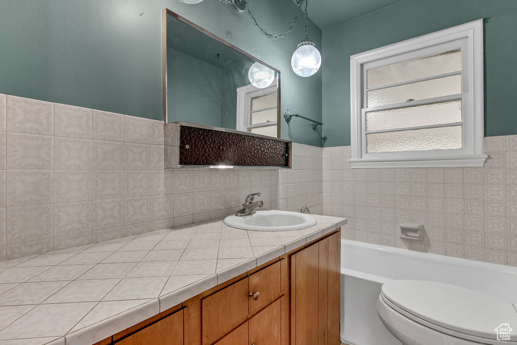 Bathroom with a tub to relax in, tile walls, vanity, and toilet