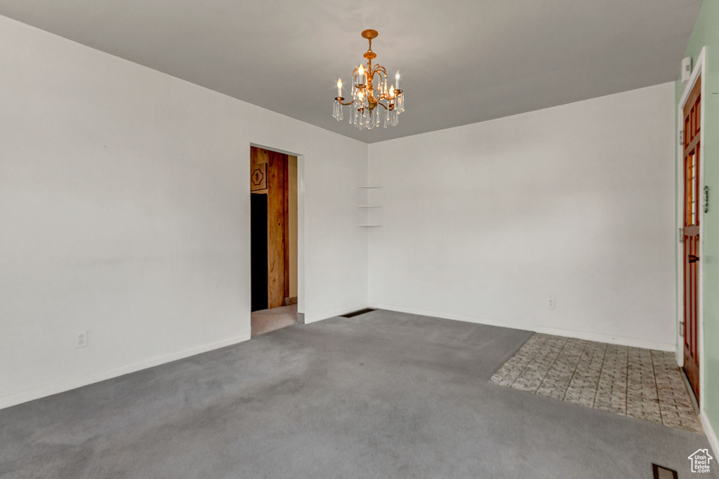 Spare room featuring dark carpet and a chandelier