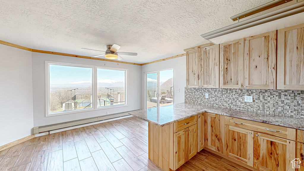 Kitchen featuring ceiling fan, light brown cabinetry, a baseboard radiator, and kitchen peninsula