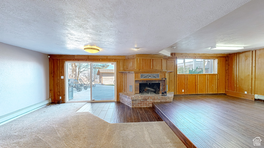 Unfurnished living room with a textured ceiling, wood-type flooring, a brick fireplace, and plenty of natural light