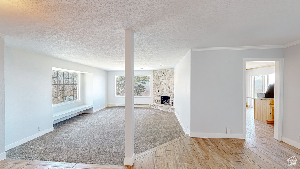 Unfurnished living room featuring ornamental molding, a textured ceiling, a fireplace, a baseboard radiator, and light wood-type flooring