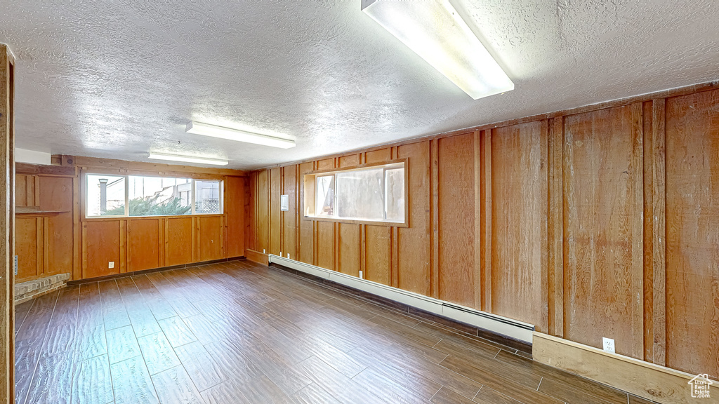 Unfurnished room featuring wooden walls, a textured ceiling, baseboard heating, and dark wood-type flooring