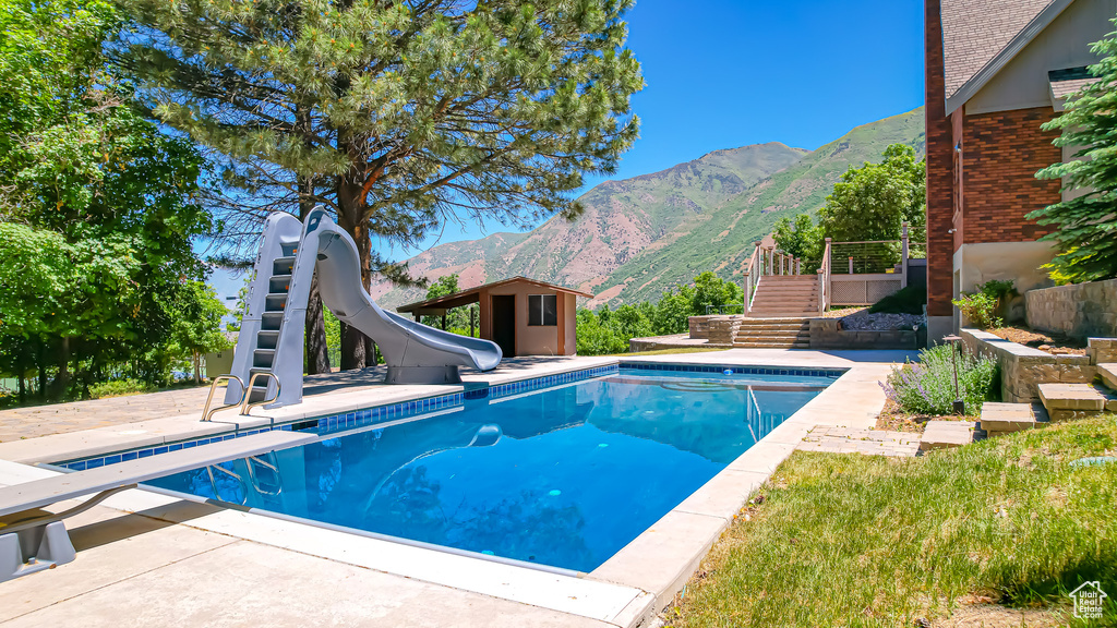 View of swimming pool featuring a mountain view, a diving board, a water slide, and a patio area