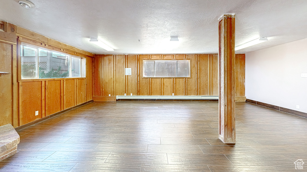 Interior space with a textured ceiling, baseboard heating, wood walls, and dark hardwood / wood-style flooring