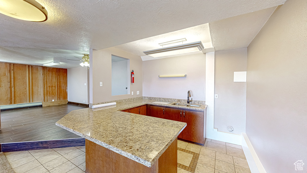 Kitchen with ceiling fan, sink, kitchen peninsula, a textured ceiling, and a baseboard heating unit