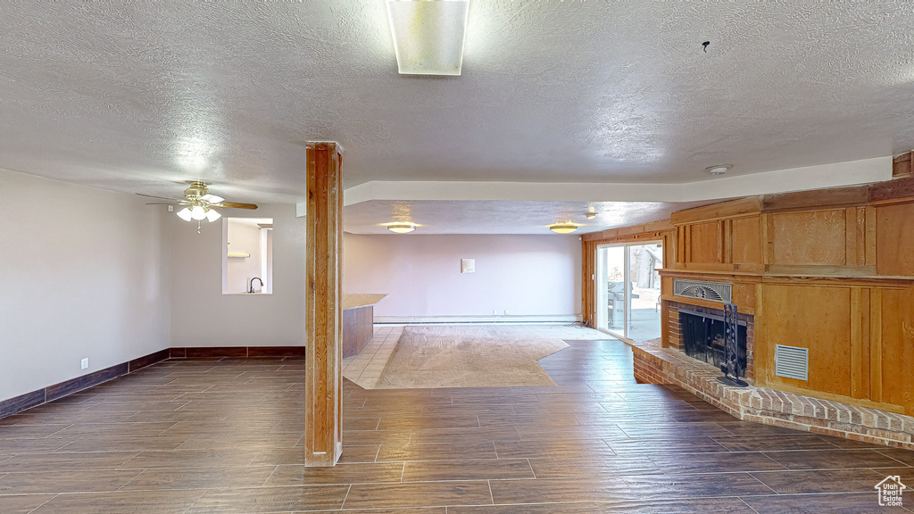 Unfurnished living room featuring a textured ceiling, ceiling fan, and a brick fireplace