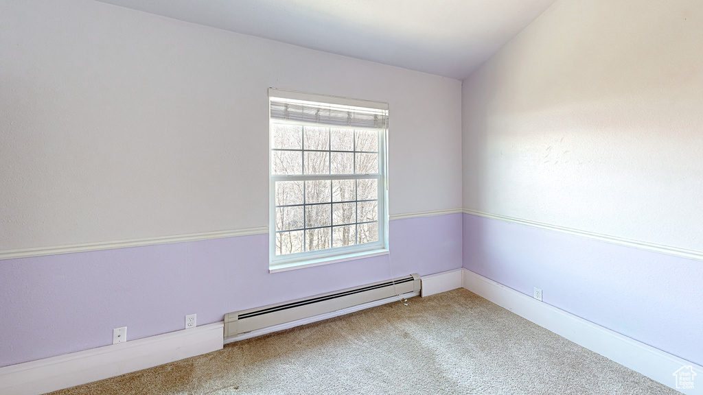 Carpeted spare room featuring vaulted ceiling and a baseboard heating unit