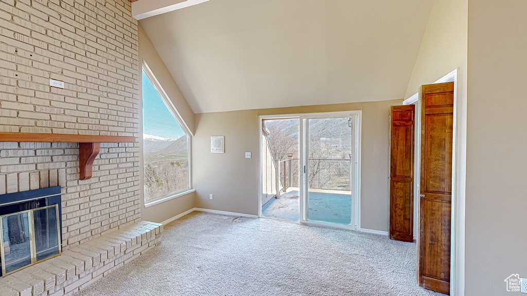 Unfurnished living room with light colored carpet, a fireplace, and high vaulted ceiling