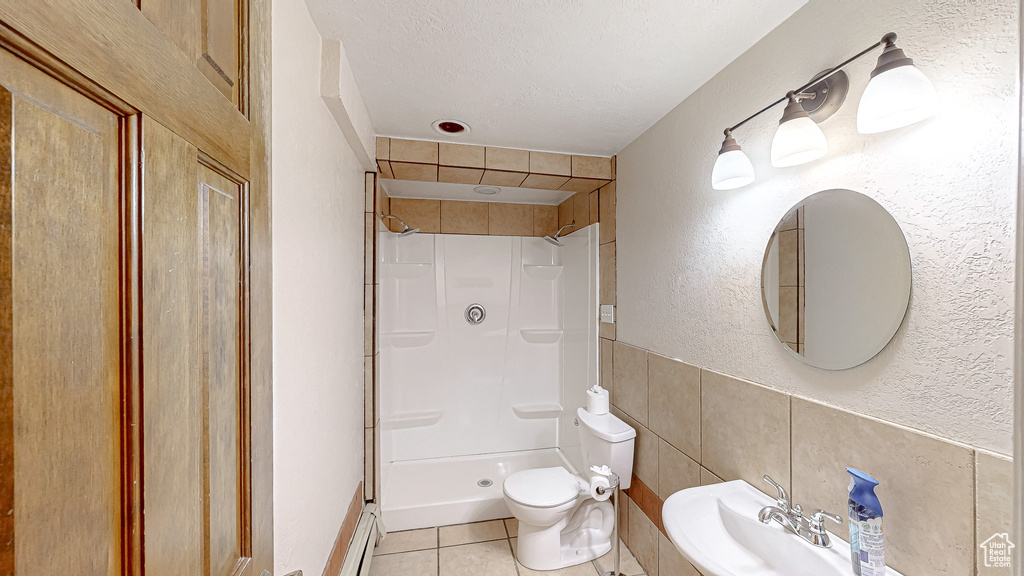 Bathroom with a tile shower, toilet, sink, and tile patterned floors