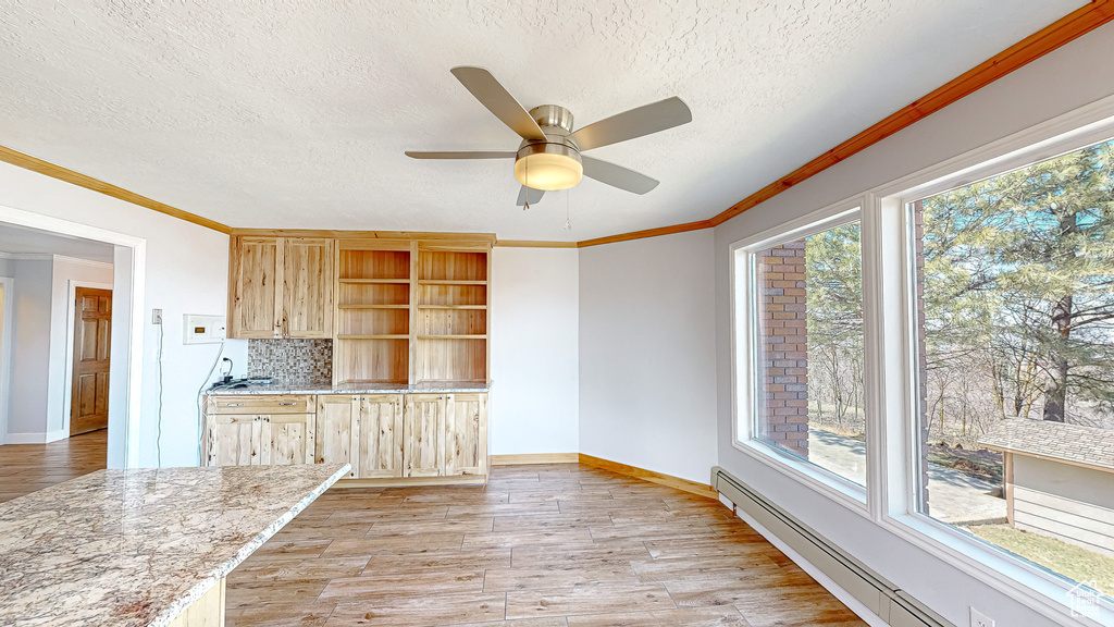 Kitchen featuring ceiling fan, light brown cabinetry, a baseboard heating unit, and a wealth of natural light