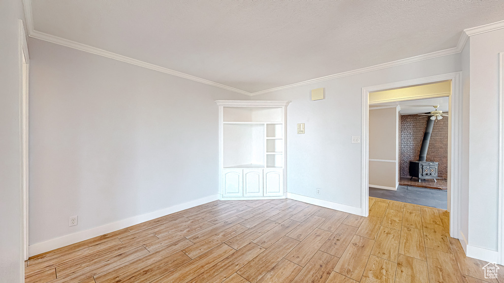 Unfurnished room featuring light wood-type flooring, ornamental molding, ceiling fan, and a wood stove