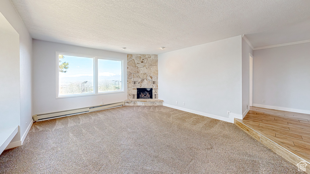 Unfurnished living room featuring a baseboard heating unit, wood-type flooring, a textured ceiling, a fireplace, and ornamental molding