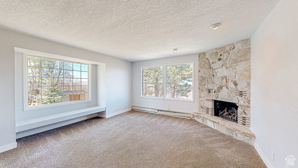 Unfurnished living room with carpet flooring, a baseboard heating unit, plenty of natural light, and a fireplace