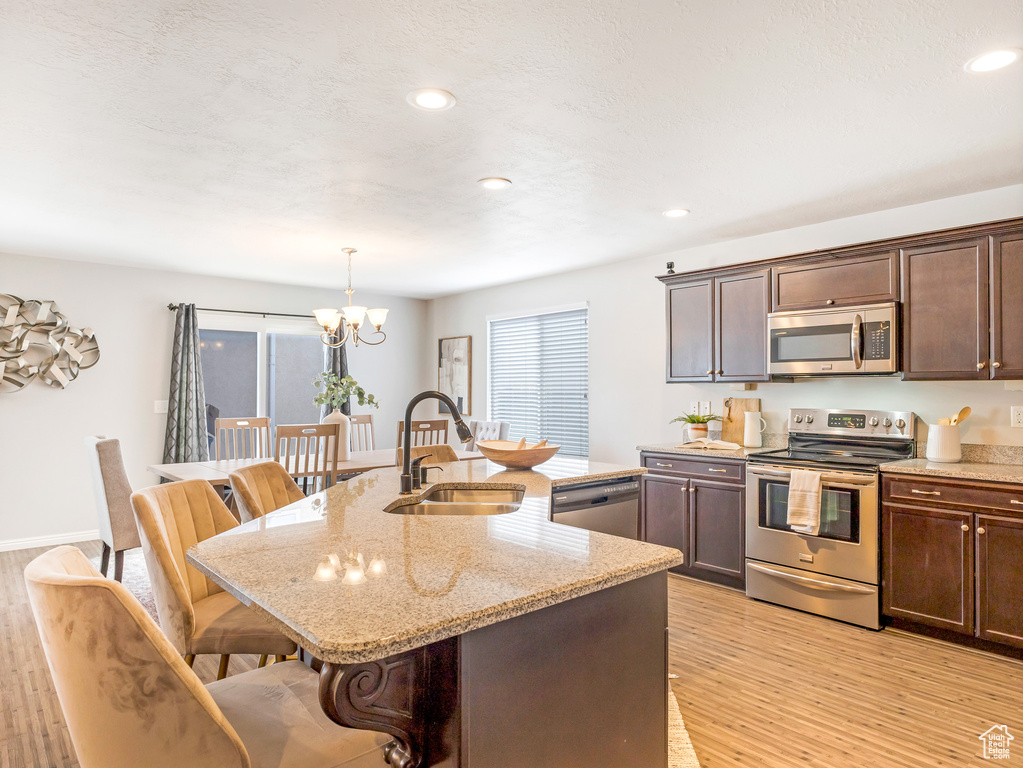 Kitchen with light hardwood / wood-style floors, a breakfast bar area, stainless steel appliances, sink, and a notable chandelier