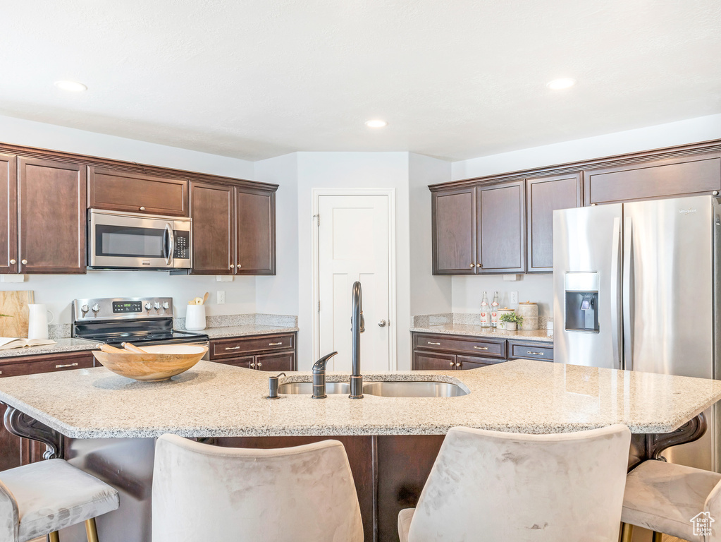 Kitchen featuring an island with sink, stainless steel appliances, light stone counters, and a breakfast bar