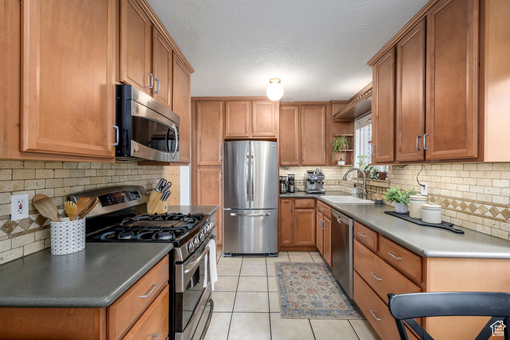 Kitchen featuring light tile patterned flooring, tasteful backsplash, stainless steel appliances, a textured ceiling, and sink