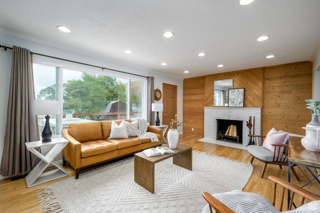 Living room with ornamental molding, light hardwood / wood-style floors, wooden walls, and a brick fireplace