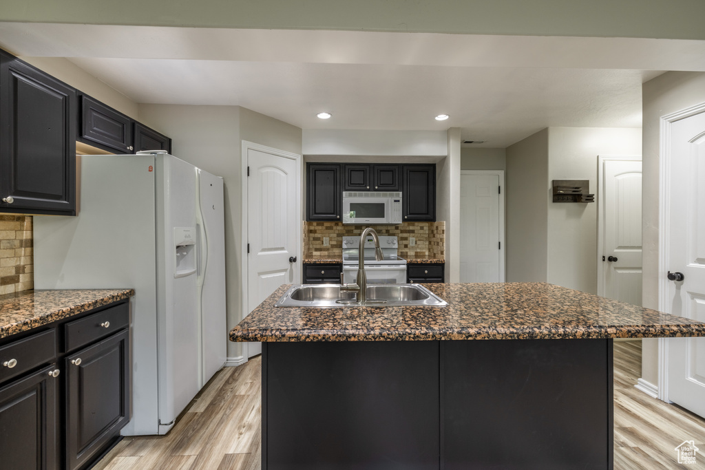 Kitchen featuring a center island with sink, light hardwood / wood-style floors, white appliances, and tasteful backsplash