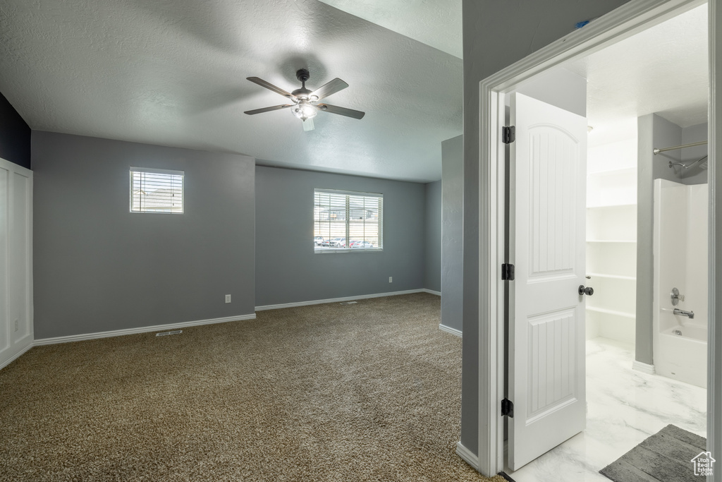 Carpeted spare room featuring a wealth of natural light, ceiling fan, and a textured ceiling