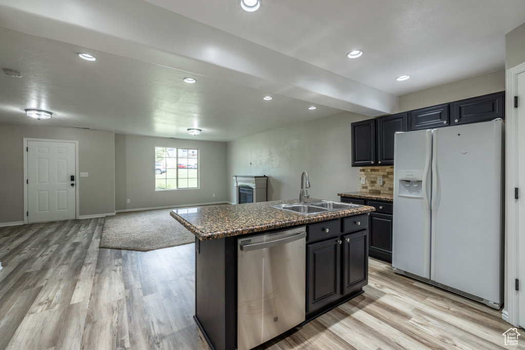 Kitchen with light hardwood / wood-style floors, white fridge with ice dispenser, stainless steel dishwasher, a kitchen island with sink, and sink