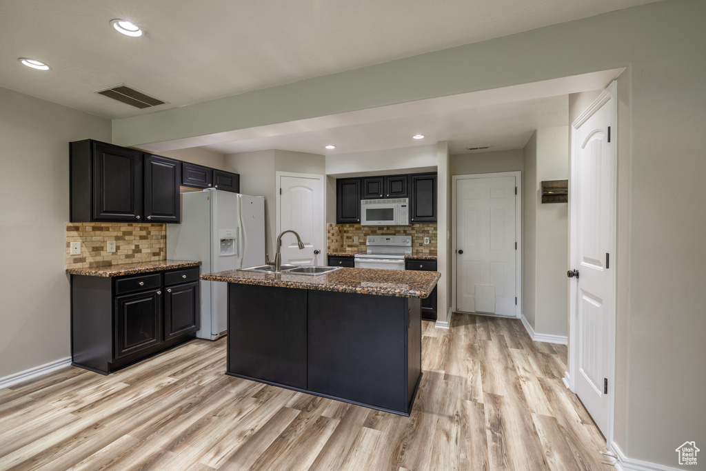 Kitchen with an island with sink, decorative backsplash, white appliances, and sink