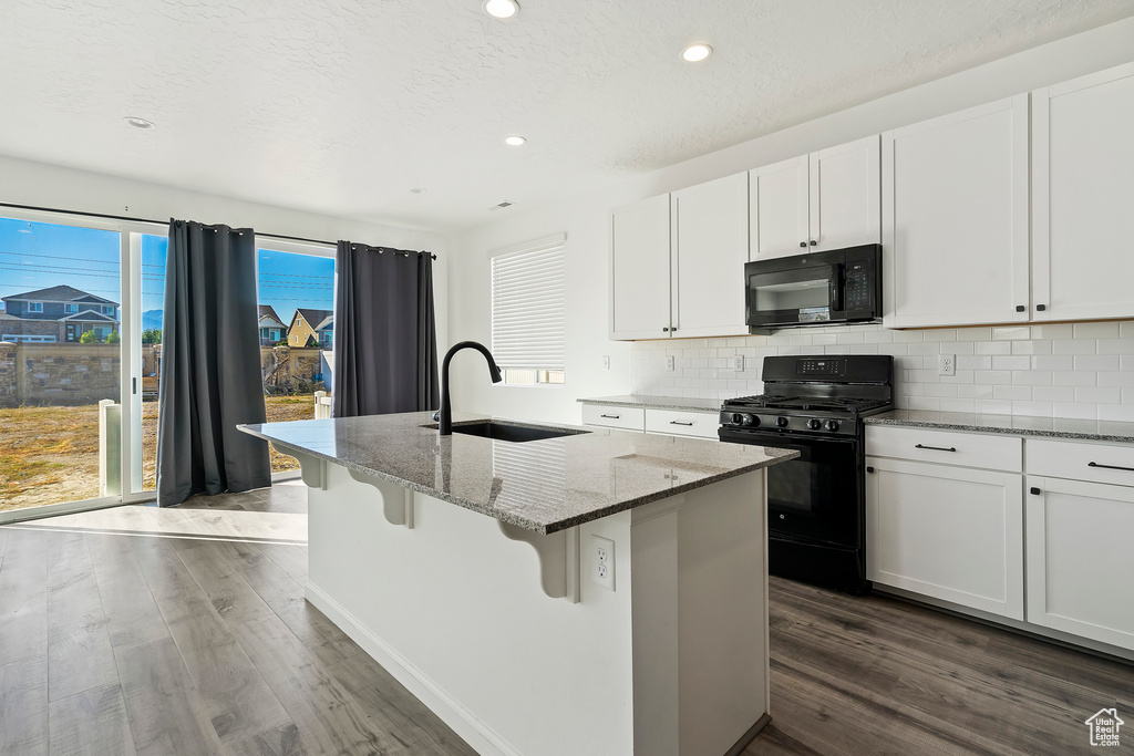 Kitchen featuring white cabinets, black appliances, a kitchen island with sink, and sink