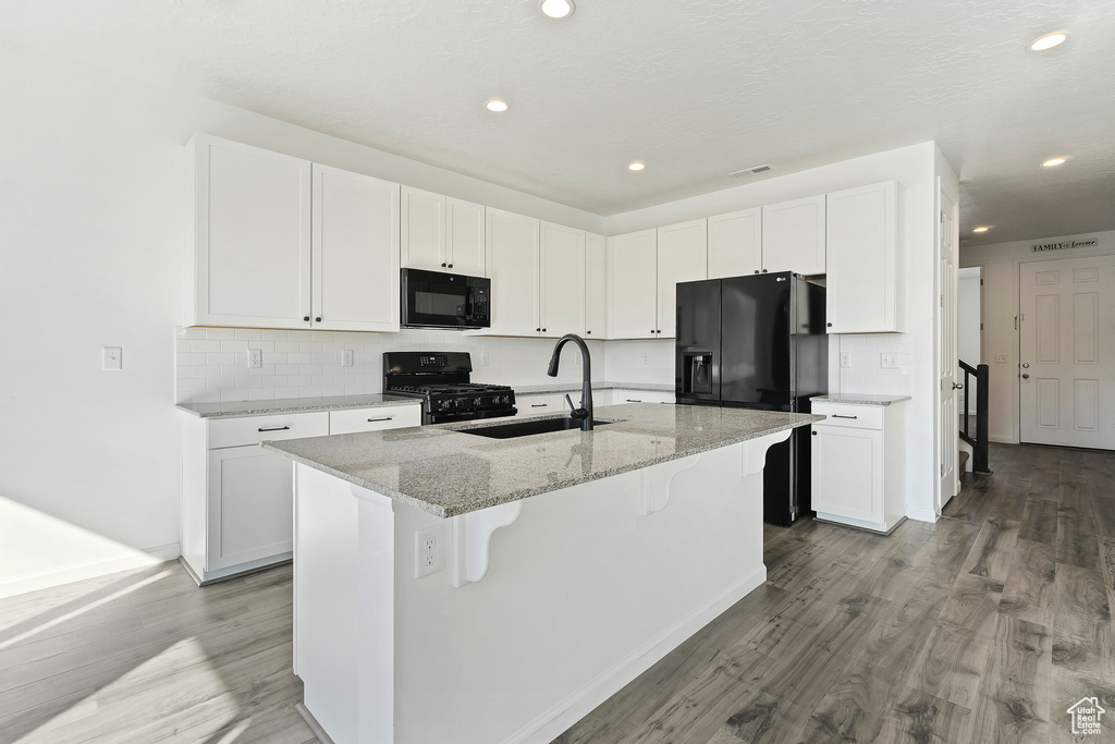 Kitchen with white cabinets, an island with sink, sink, black appliances, and hardwood / wood-style floors