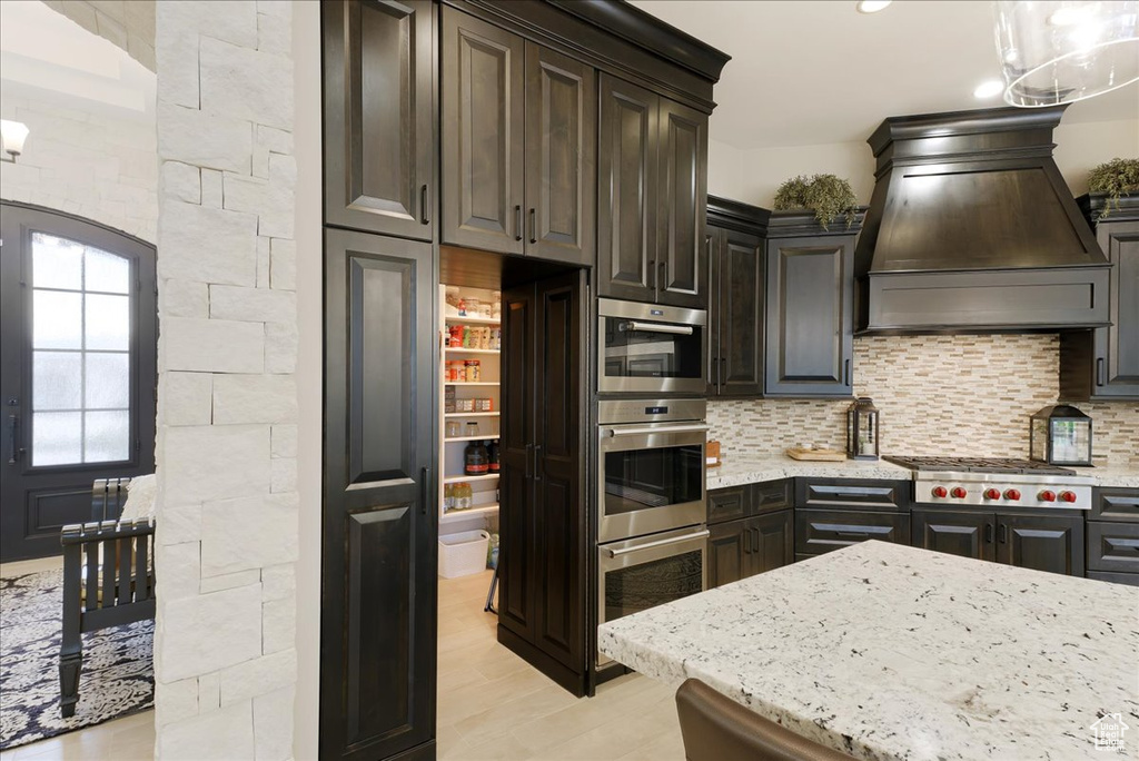 Kitchen featuring backsplash, appliances with stainless steel finishes, decorative light fixtures, and custom exhaust hood