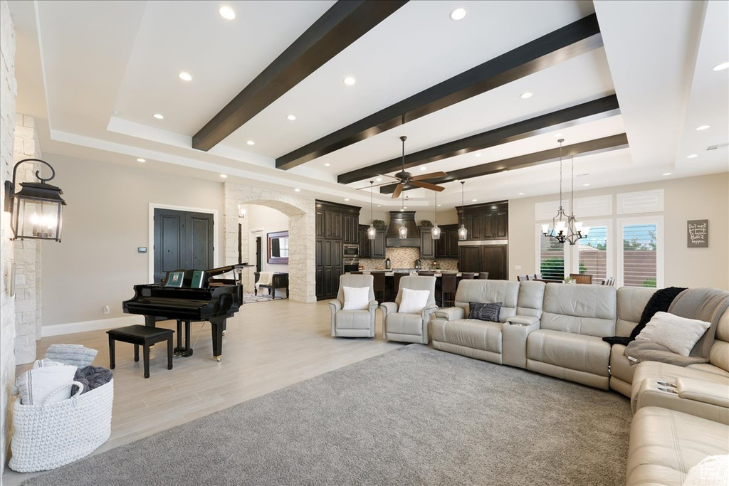 Living room with light hardwood / wood-style floors, ceiling fan with notable chandelier, a fireplace, beam ceiling, and a tray ceiling