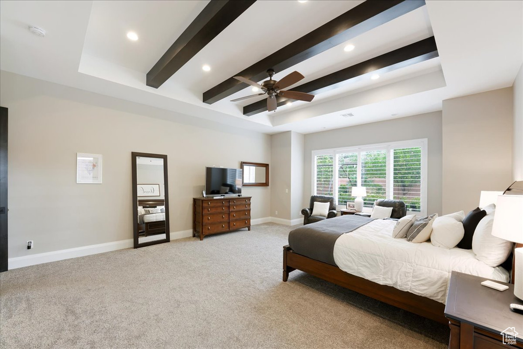 Bedroom with a tray ceiling, beam ceiling, ceiling fan, and light colored carpet